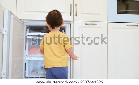 The child is playing near the open door of the freezer. The baby is looking at the white fridge, wondering what's inside. Kid aged about two years (one year ten months)