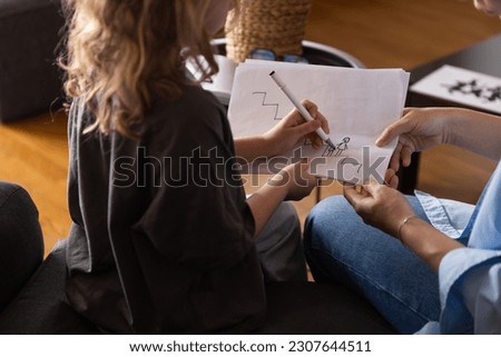 A girl at a psychologist's appointment draws a test drawing, low self-esteem and psychological problems in a child, a photo from the back. High quality photo