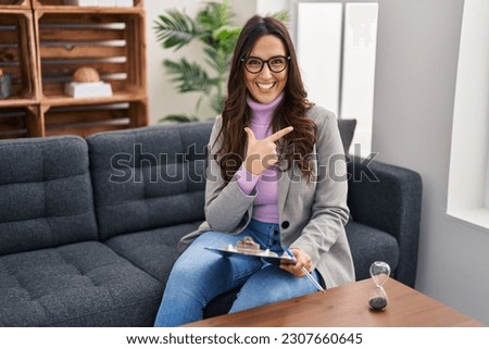 Young brunette woman working at consultation office cheerful with a smile on face pointing with hand and finger up to the side with happy and natural expression 