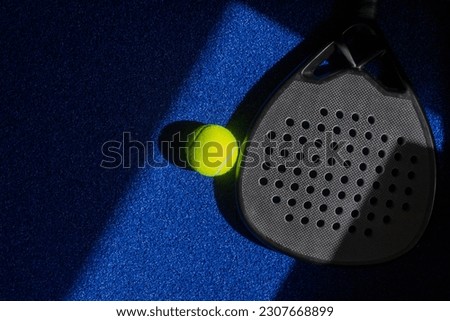 Black professional paddle tennis racket and ball with natural lighting on blue background. Horizontal sport theme poster, greeting cards, headers, website and app