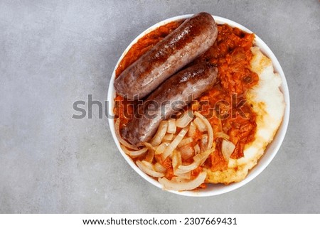 Traditional South African Pap and Wors, sausage with popular maize meal staple covered with Chakalaka or relish on mottled gray with copy space Royalty-Free Stock Photo #2307669431