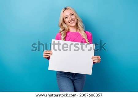 Photo of positive optimistic girl wavy hairdo dressed pink sweater holding white placard empty space isolated on blue color background