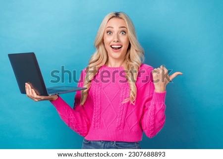Photo of impressed astonished girl dressed knit sweater indicating empty space offer hold laptop isolated on blue color background