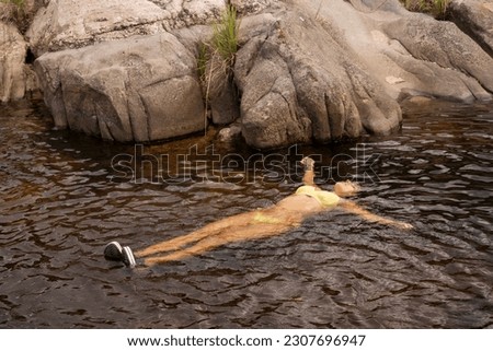Relaxing in vacations. Portrait of a woman in her 20s, wearing a yellow bikini, resting in the river. 