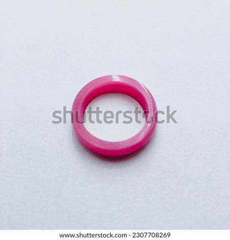 A circular shape pink colour ring on white background. It is made of resin material. It is really normal ring and look like comfortable. It is so pretty and simple ring. Beautiful charm ring.Love it