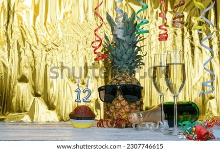Cheerful pineapple in glasses festive happy birthday character with number  12. Beautiful background for congratulations copy space on a golden background with glasses of champagne. Anniversary 