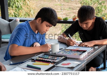 Asian boys are spending their free times with drawing, sketching, coloring and painting by using watercolor bars in cases, teenagers activity in summer and watercolor lesson concept.