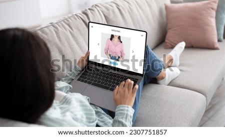 Millennial indian woman with laptop lying on sofa and shopping online remotely from home, look at clothes at screen. Young lady customer enjoy spare time, shopaholic ordering purchases Royalty-Free Stock Photo #2307751857
