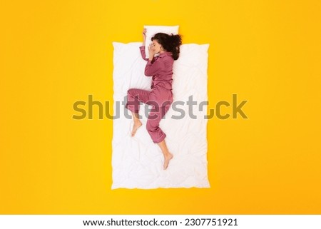 Dreamy Nights. Peaceful Lady In Pajamas Sleepwear Drifting in Sleep Lying On Blanket Hugging Pillow On Yellow Studio Background, Above View Shot. Restful Beauty Sleep Concept Royalty-Free Stock Photo #2307751921