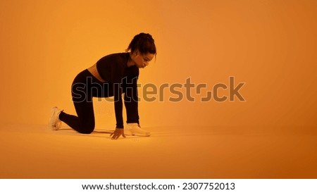 Sport motivation concept. Determined black sportswoman ready for race posing in crouch start position on orange neon background, panorama with free space