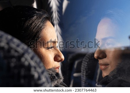 Colombian woman traveling by bus, looking out the window, smiling and her face reflected in the glass. Royalty-Free Stock Photo #2307764463