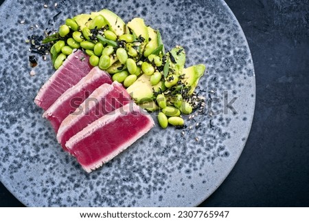 Modern style traditional Japanese gourmet seared tuna fish steak tataki with avocado fruit and edamame soy beans served as top view on a Nordic design plate with copy space right  Royalty-Free Stock Photo #2307765947