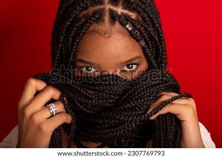 Close-up portrait of black woman with holding her braids to her face. Isolated on red background Royalty-Free Stock Photo #2307769793