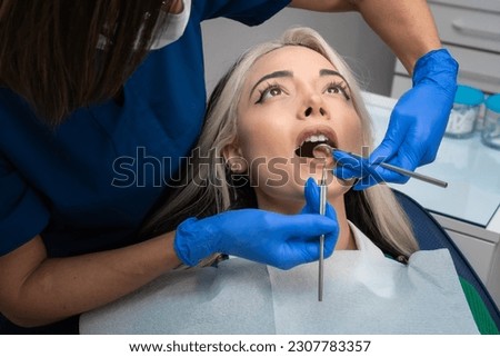 Stomatologist checkup. Close-up of a young woman with her mouth open, a dentist with the help of dental equipment makes an examination of the oral cavity Royalty-Free Stock Photo #2307783357