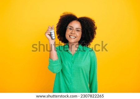 Joyful happy african american or brazilian beautiful woman with curly hair, wearing green shirt, holding car key in hand, rejoices in new purchase, smile at camera, stand on isolated orange background