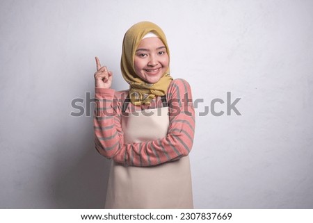 Portrait of smiling housewife woman in hijab and apron looking at camera, finger on the head, having a great idea isolated on white background. People housewife muslim lifestyle concept
