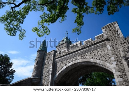 Historic stone arch with towers, turrets, and crenelations. Upward wide angle view of historic landmark framed by trees against a clear blue sky. Royalty-Free Stock Photo #2307838917