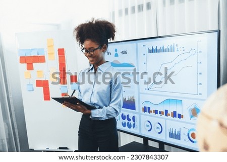 Young african businesswoman presenting data analysis dashboard on TV screen in modern meeting. Business presentation with group of business people in conference room. Concord Royalty-Free Stock Photo #2307843307