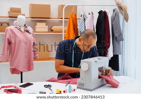 Photo of stylish and fashionable clothes asian designer man sews at a sewing machine. Sewing, design work, tailoring studio, tailor, designer clothes, manufactory