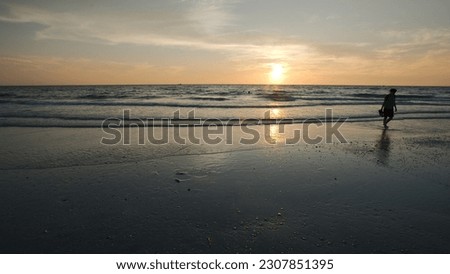 silhouette of man  at Florida beach at sunset with blue sky and yellow colors with water and sand.. Taking pictures of sunset with cell phone . Sun on edge of horizon.