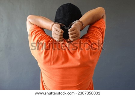 Rear view of a prisoner in orange t-shirt wearing handcuff isolated over grey background