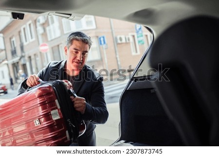 Middle aged man putting a suitcase in the trunk of a car Royalty-Free Stock Photo #2307873745