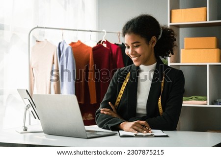 African american designer woman checking details clothes of customer on laptop and writing notes.