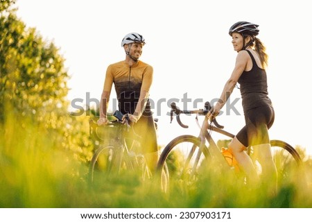Portrait of a couple of athletes taking a break or preparing for a race on their bikes. Healthy lifestyle. Professional road bicycle racers in action. Concept of endurance and strength. Copy space. Royalty-Free Stock Photo #2307903171