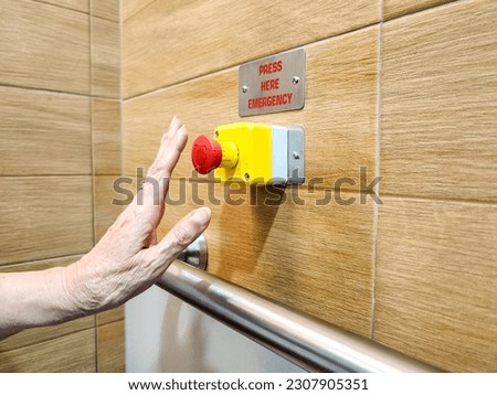 hand of senior woman press Red emergency button with handrail on wall in the disabled toilet. Security and assistance for disabled, senior concept.