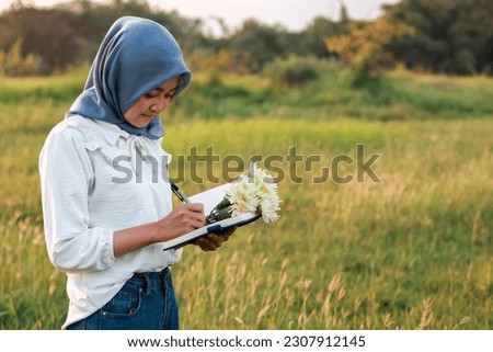 portrait of a Muslim woman writing in a book. woman in hijab writing while standing outdoors with negative space concept.