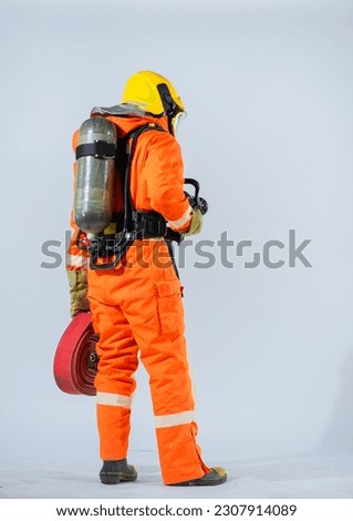 Vertical picture of the professional firefighter is standing with his back turned holding a fire hose and wearing an oxygen tank on his back while looking sideways on a white background