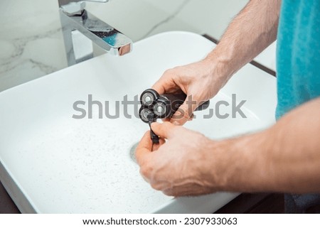 Man cleaning dirty shaver with brush. Details of shaver head and cleaning brush on light background Royalty-Free Stock Photo #2307933063