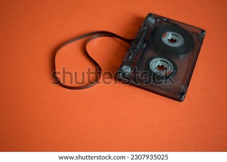Audio cassette with stretched tape on orange background.