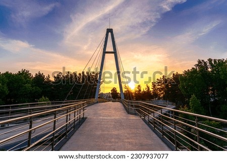 Modern footbridge with steel cables across the Anhor canal in Navruz park at sunset in summertime, Uzbekistan, Tashkent.