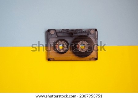 Audio cassette in the middle on a blue and yellow background, top view.