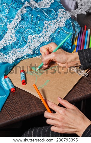 Fashion designer draws a sketch of the future dress on paper, beside lie thread and lace