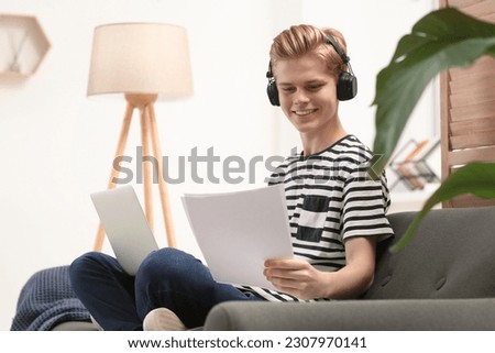 Online learning. Smiling teenage boy with laptop looking on essay at home