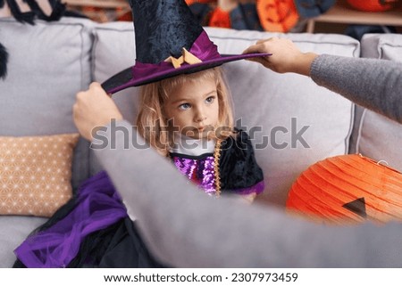 Adorable blonde girl wearing hat witch costume having halloween party at home