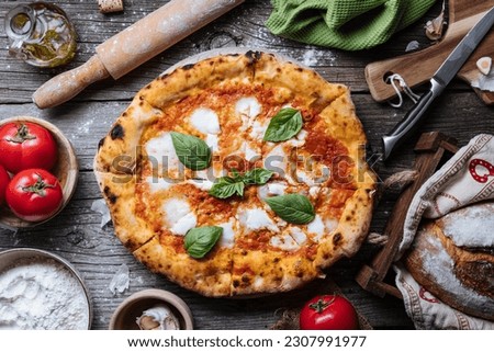 Pizza Napoletana, traditional and authentic Italian pizza baked in wood fired oven. Margherita pizza with mozzarella cheese, tomato sauce, olive oil and basil leaves. On wooden board with ingredients.
