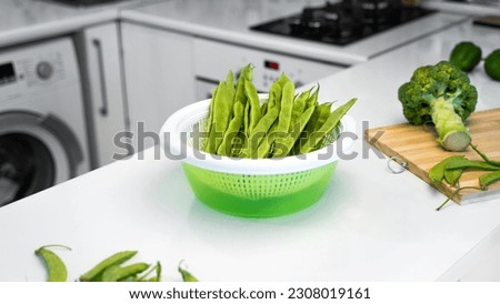 The concept of a healthy nutrition and vegetarian lifestyle. Modern kitchen interior with green vegetables, romano helda beans, green peas and broccoli on the table. Bright white kitchen. Copy space.