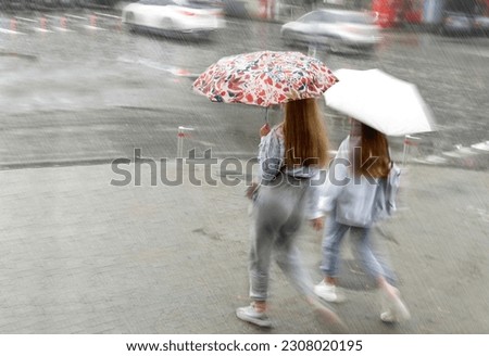 Blurred image of two girls with umbrella walking in the rain down the street