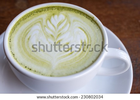 A cup of hot green tea with latte milk art.