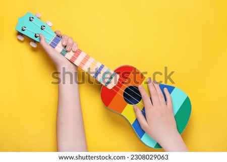 Woman holding ukulele on yellow background, closeup. String musical instrument