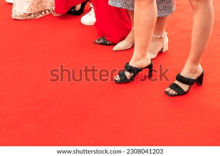 Feet of an event guests, girls stand on a red carpet, close-up photo