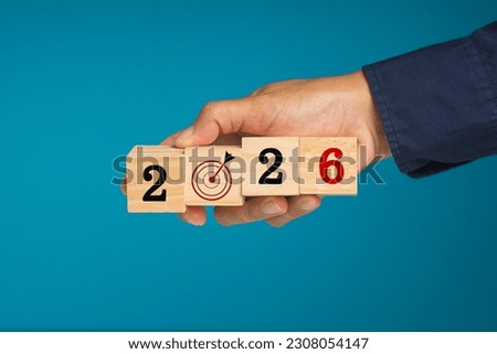 Countdown to 2026 and business planning and strategy. Hand businesspeople holding wooden cubes with the letters 2026 and dartboard against a blue background Royalty-Free Stock Photo #2308054147