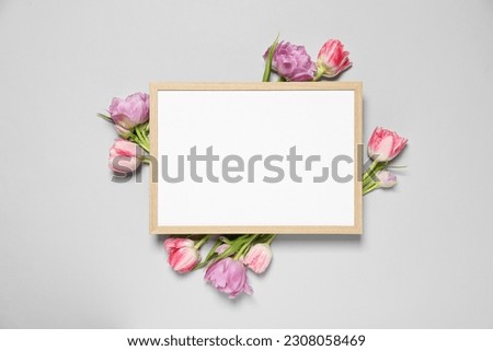 Empty photo frame and beautiful flowers on light gray background, top view. Space for design