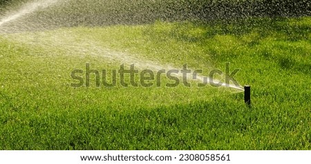Automatic garden irrigation system watering lawn. Savings of water from sprinkler irrigation system with adjustable head. Automatic equipment for irrigation and maintenance of lawns, gardening. Banner Royalty-Free Stock Photo #2308058561