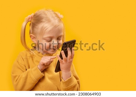 Child with smartphone in hands. Little girl scrolling feed on smart phone or plays in game, yellow background