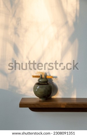 Small round green ceramic urn on shelf set against wall with tree branches shadows Royalty-Free Stock Photo #2308091351