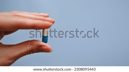 capsule between the fingers on a blue background, medication, medical worker's day, medical care, banner for the hospital